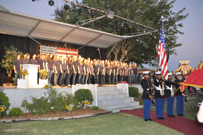 choir on stage and four men in uniform in front of stage with american flag