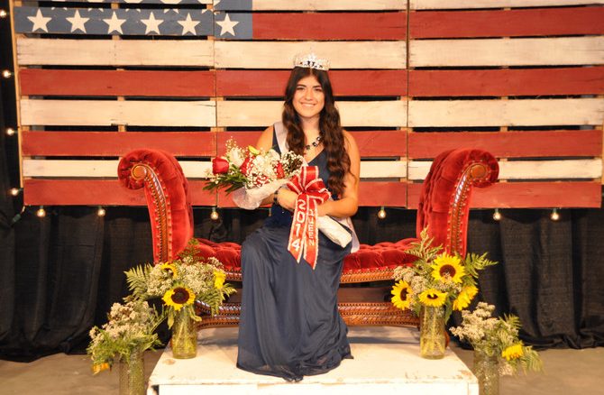 girl with crown and bouquet of flowers sitting in front of american flag