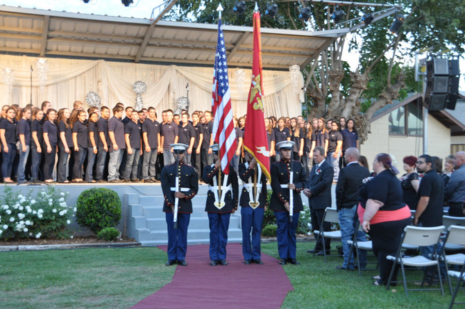 choir standing on stage and men in uniform standing in front of stage with flags and guns