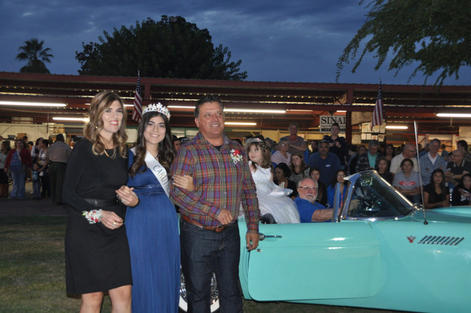 girl with crown linking arms with parents in front of classic convertible car