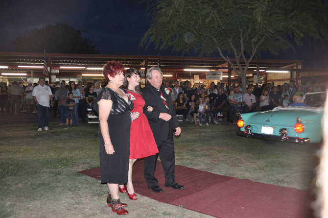 girl linking arms with parents in front of classic convertible car