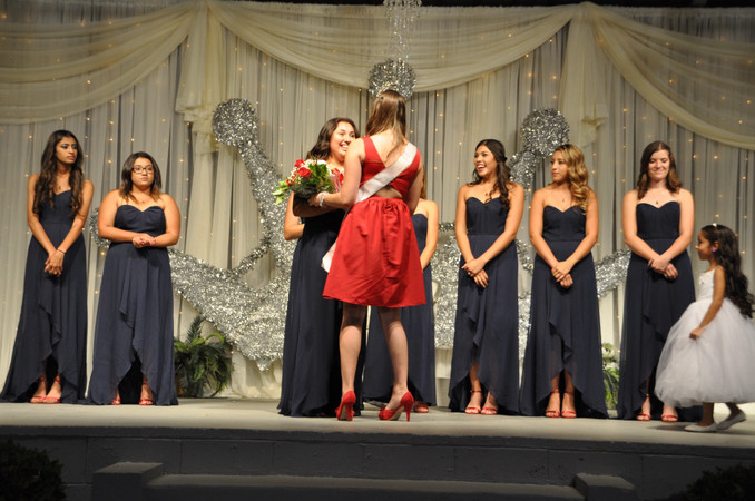 girl handing bouquet of flowers to queen contestant on stage