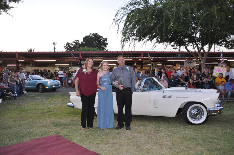 girl linking arms with parents in front of classic car