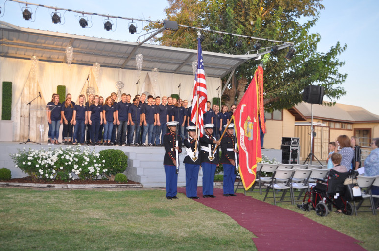 choir singing on stage and men in uniform with american flag in front of the stage