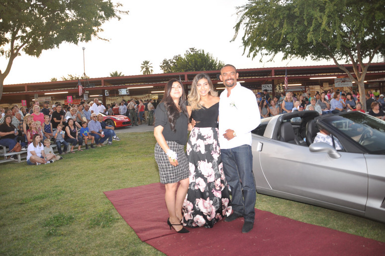 girl standing with parents in front of sports car