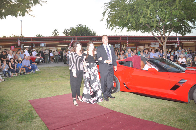 girl standing with parents in front of red sports car