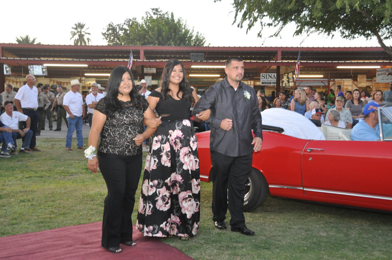 girl standing with parents in front of red classic car